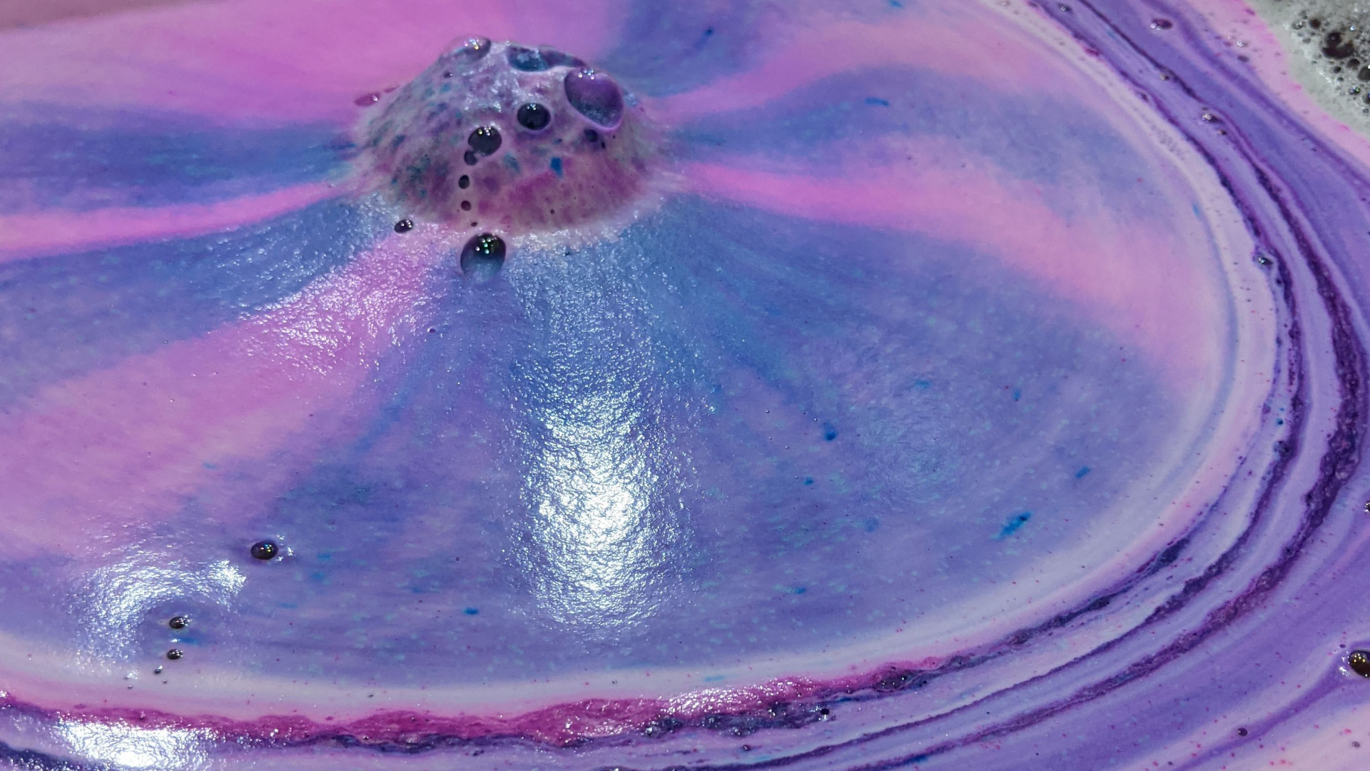 close up photo of a bath bomb in the water transforming the color into violet, lilac and soft blue pastel hues. 